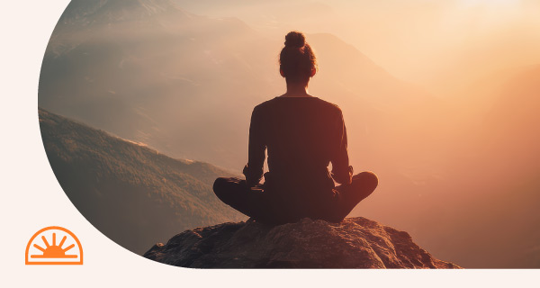A woman sitting outside, meditating in the sunset.